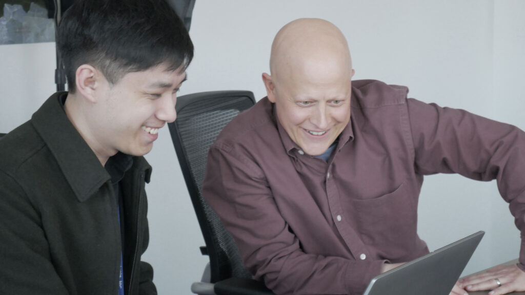 Two SPA employees smiling as they look down at a laptop screen
